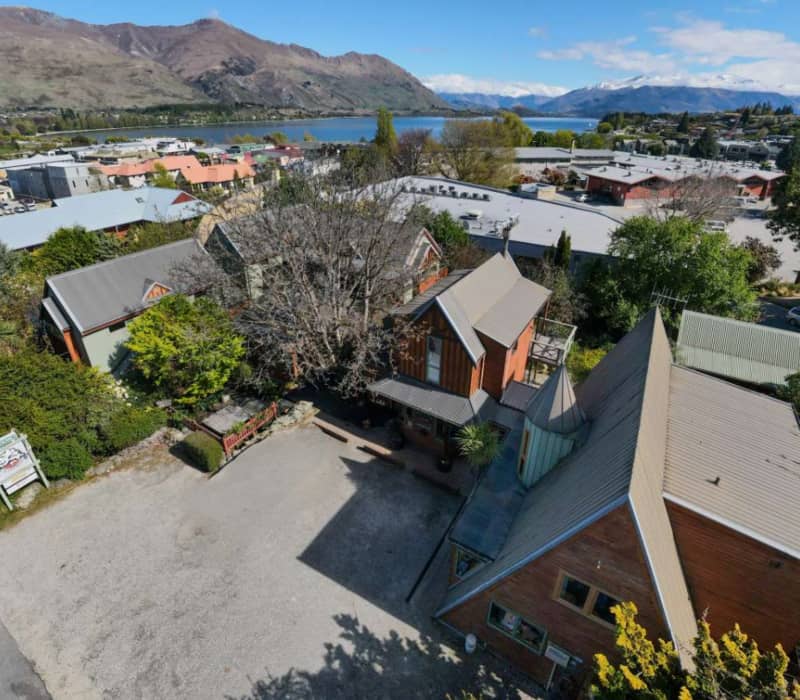 An elevated aerial view of a timber-clad lodge complex nestled near a blue lake and rugged mountains. Credit: Te Wanaka Lodge
